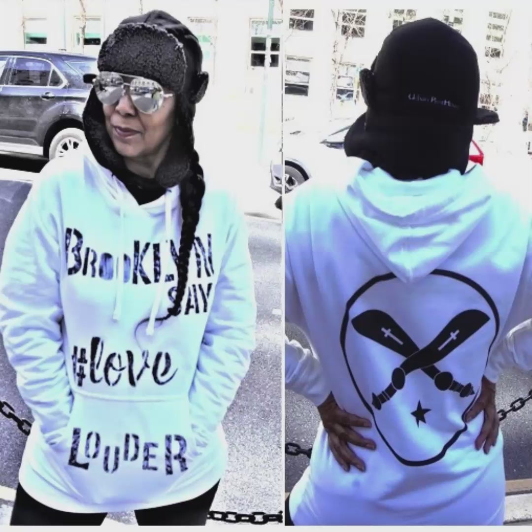 Woman wearing white essential graphic hoodie, hand-painted Brooklyn Says Love Louder in black, and logo on back of white hoodie print in black.
