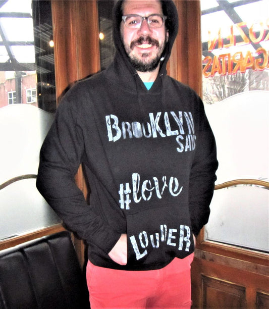 Man wearing black essential graphic hoodie, hand-painted Brooklyn Says Love Louder in white.