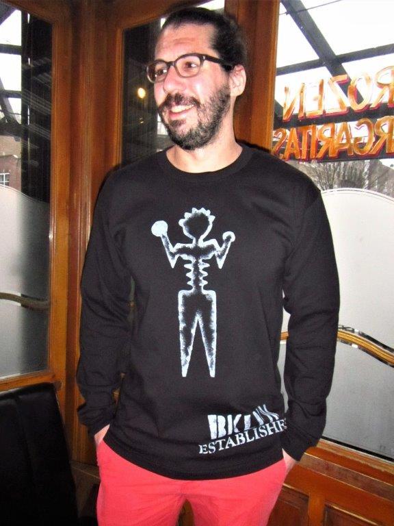 Man wearing champion long sleeve black graphic tee shirt, artist ambiguous person with Brooklyn established words painted in white.