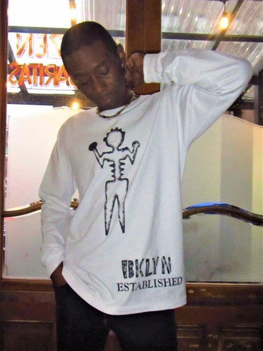 Man wearing champion long sleeve white graphic tee shirt, artist ambiguous person with Brooklyn established words painted in black.