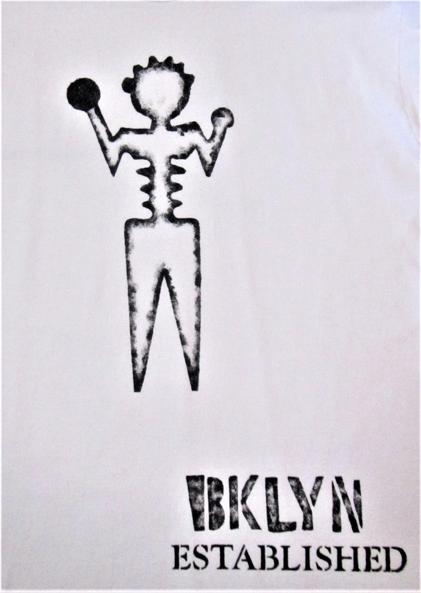 Close up of black hand-painted ambiguous person with Brooklyn established words on white tee shirt.