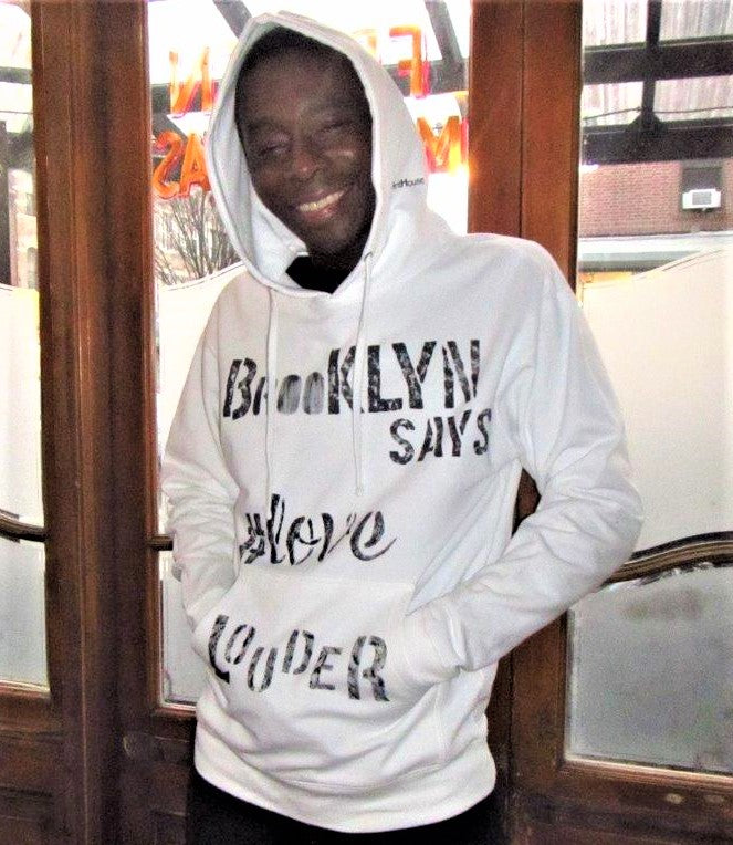 Man wearing white essential graphic hoodie, hand-painted Brooklyn Says Love Louder in black.