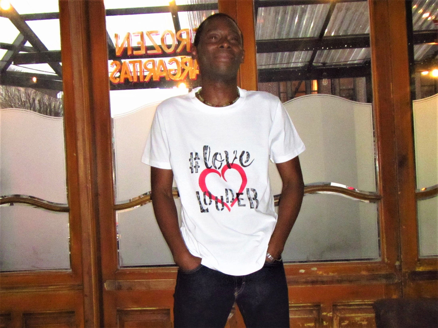 Man wearing white short sleeve graphic tee shirt, hand-painted Love Louder in black with a large red heart centered on the front.