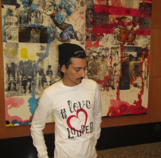 Man wearing white long sleeve tee shirt, hand-painted Love Louder in black with a large red heart centered on the front. 