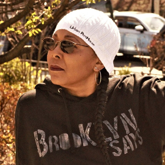 Woman wearing white fitted Cable Knit cap with Urban PentHouse embroidery in black.