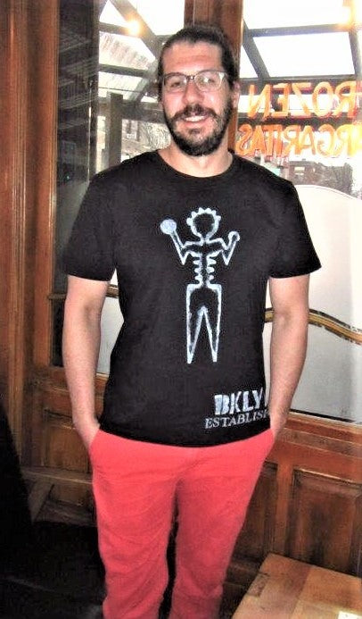 Man wearing champion short sleeve black graphic tee shirt, artist ambiguous person with Brooklyn established words painted in white.